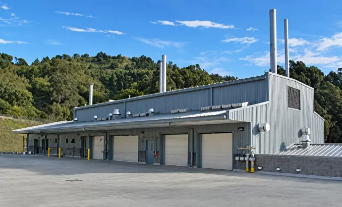 Building 85 Waste Handling Facility at Lawrence Berkeley National Laboratory in Berkeley, California: a metal-clad building with roll-up loading bay doors and exhaust stacks below the wooded Berkeley hills